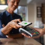 Mature woman paying bill through smartphone using NFC technology in a restaurant. Satisfied customer paying through mobile phone using contactless technology. Close up hands of mobile payment at a coffee shop.