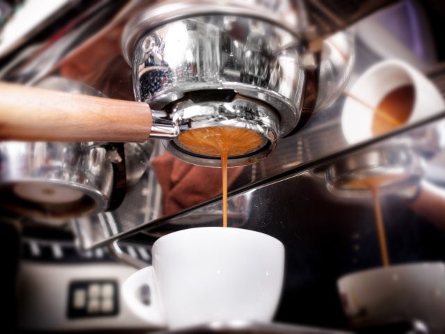 Macro shot of preparing espresso on professional coffee machine in coffeeshop or cafe closeup. Pouring strong coffee in small white cup