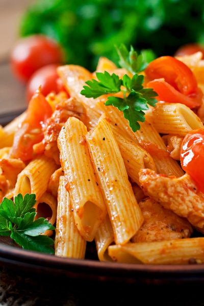 Penne pasta in tomato sauce with chicken, tomatoes on a wooden background